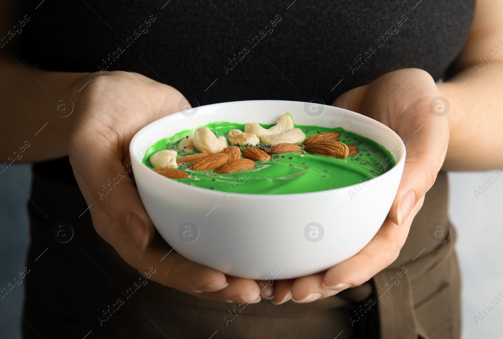 Photo of Woman holding bowl of spirulina smoothie with nuts and chia seeds, closeup