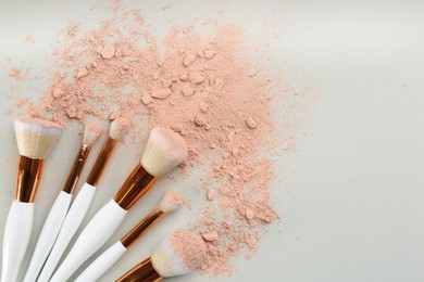 Photo of Makeup brushes and scattered face powder on light grey background, flat lay. Space for text