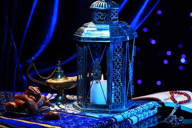 Photo of Arabic lantern, Quran, misbaha, Aladdin magic lamp, dates and folded prayer mat on mirror surface against blurred lights at night