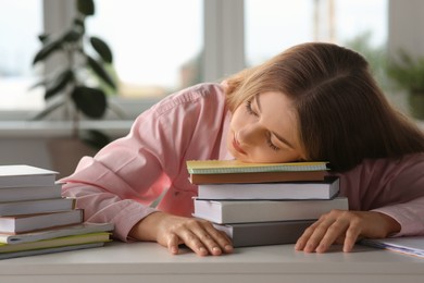 Photo of Young tired woman sleeping near books at white table indoors