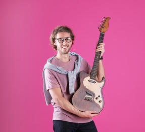Young man with electric guitar on color background