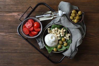 Photo of Delicious burrata cheese served with olives, croutons, basil and tomatoes on wooden table, top view