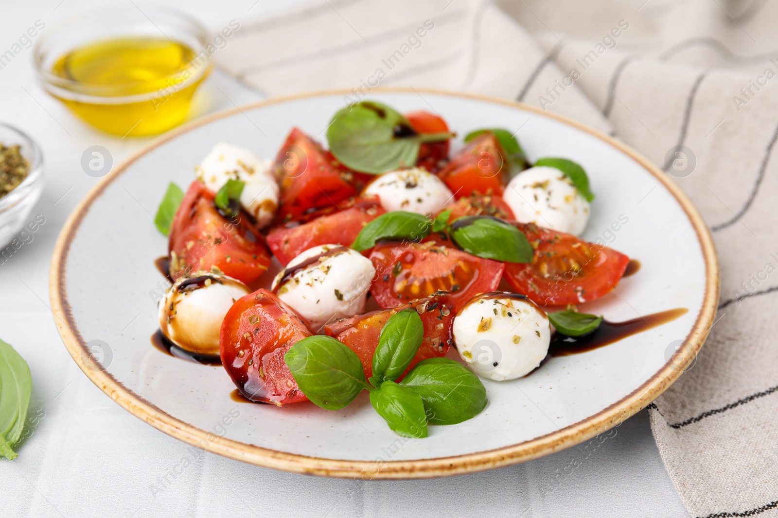 Photo of Tasty salad Caprese with mozarella balls, tomatoes, basil and sauce on white tiled table, closeup