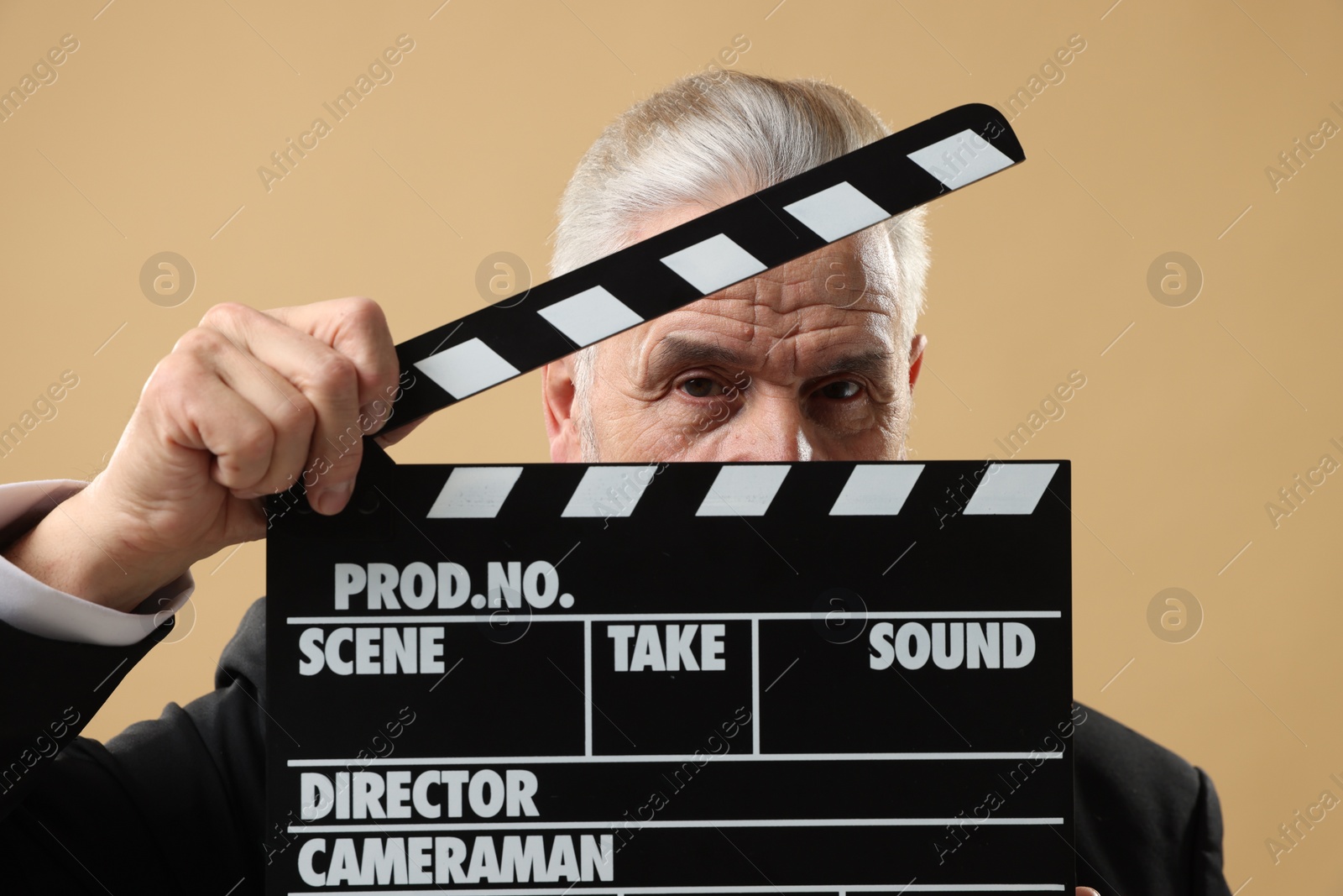 Photo of Senior actor holding clapperboard on beige background. Film industry