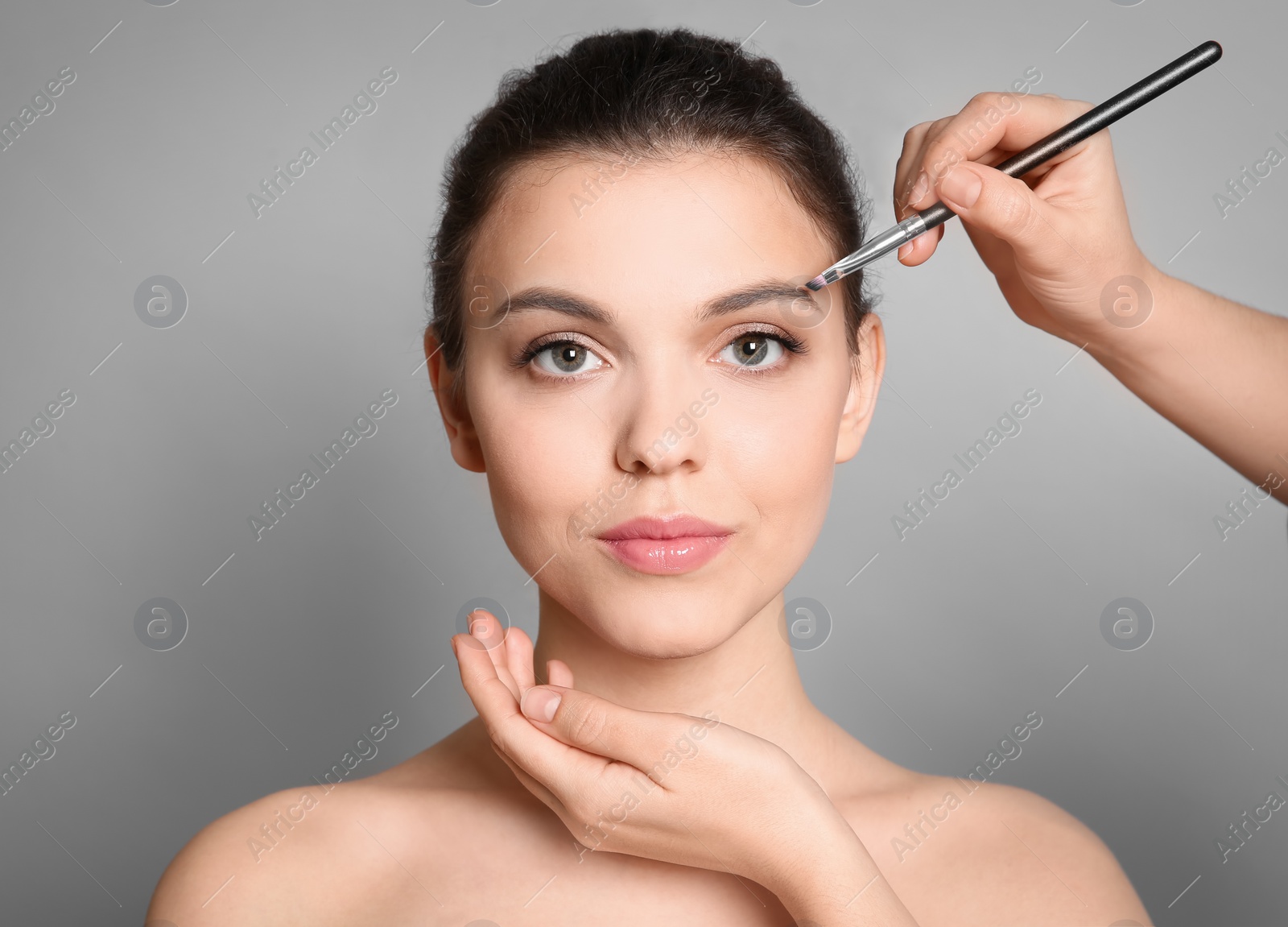 Photo of Visage artist applying makeup on woman's face against grey background. Professional cosmetic products