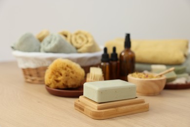 Photo of Soap bar, sponge and bottles of essential oils on light wooden table. Spa therapy