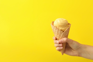 Photo of Woman holding waffle cone with delicious ice cream on yellow background, closeup. Space for text