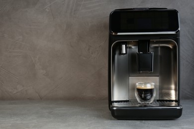 Photo of Modern espresso machine with glass of coffee on grey table, space for text