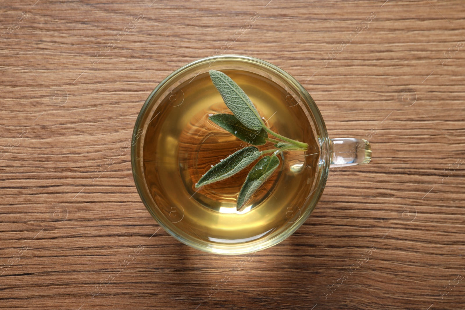 Photo of Cup of sage tea and green leaves on wooden table, top view