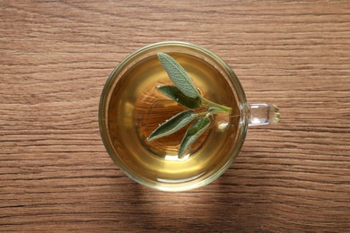 Cup of sage tea and green leaves on wooden table, top view