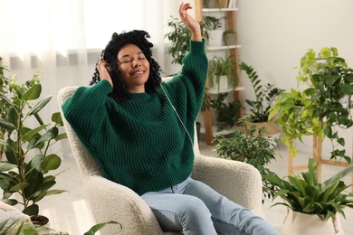 Photo of Relaxing atmosphere. Happy woman in headphones listening music and chilling surrounded by beautiful houseplants at home