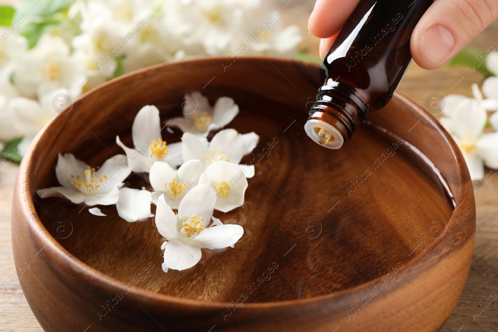 Photo of Woman dripping jasmine essential oil into wooden bowl on table, closeup