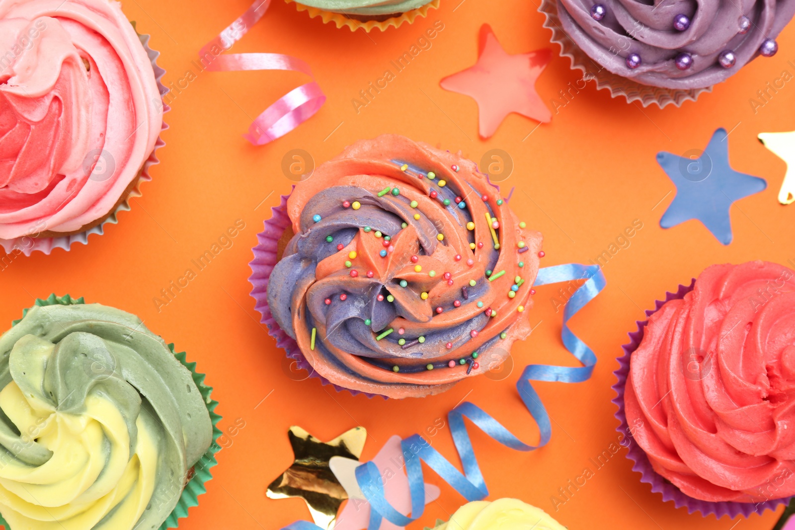 Photo of Delicious cupcakes with bright cream and party decor on orange background, flat lay