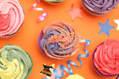 Photo of Delicious cupcakes with bright cream and party decor on orange background, flat lay