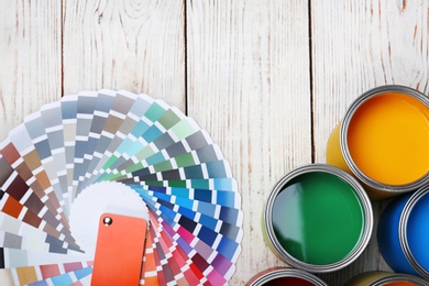 Cans with paint and color palette on wooden background, top view