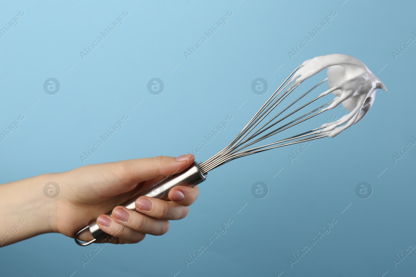 Photo of Woman holding whisk with whipped cream on light blue background, closeup