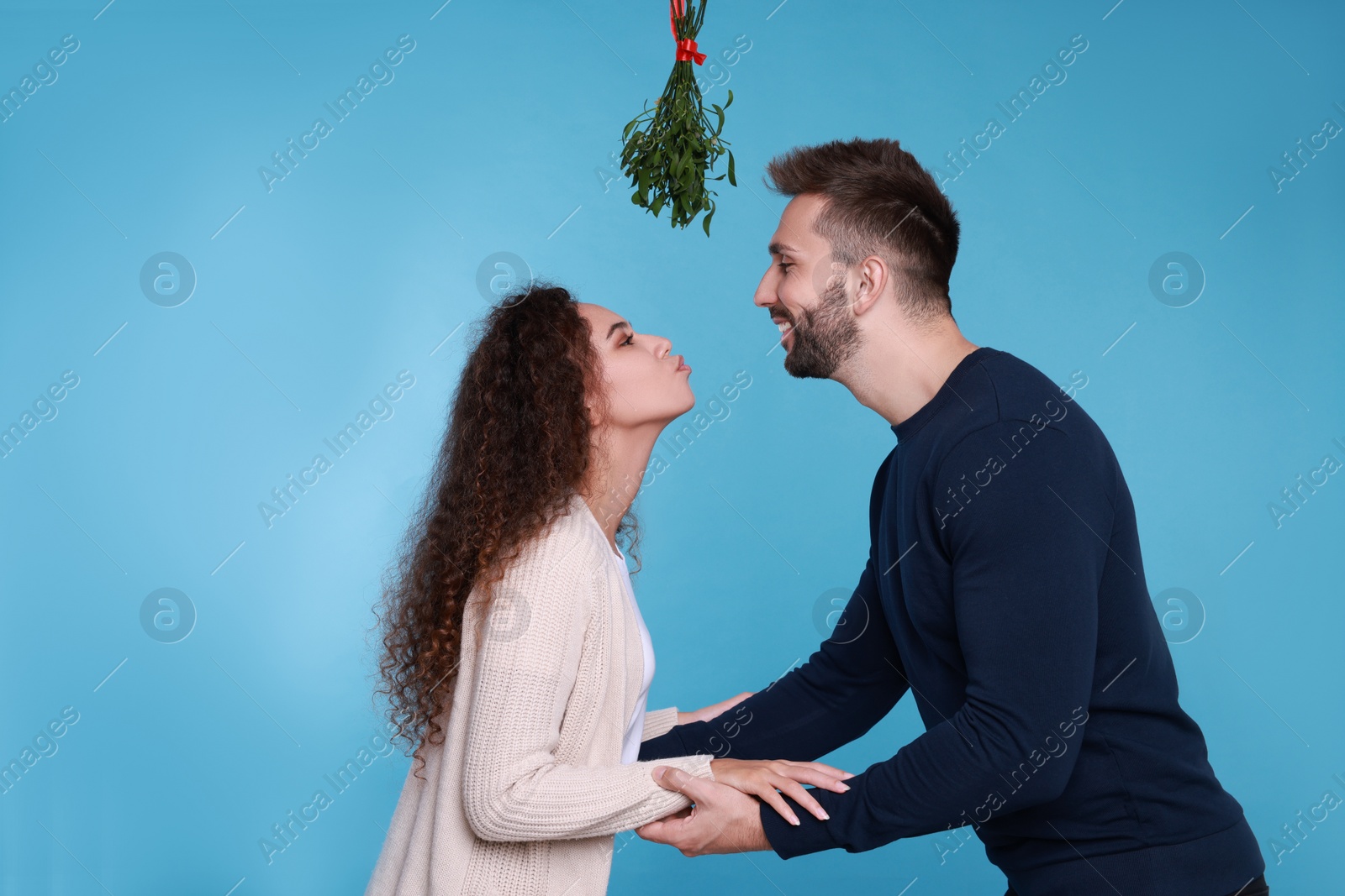 Photo of Lovely couple under mistletoe bunch on light blue background