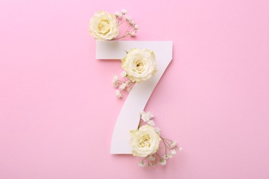 Photo of Paper number 7 and beautiful flowers on pink background, top view