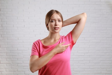 Young woman with sweat stain on her clothes against brick wall. Using deodorant