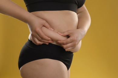 Woman touching belly fat on goldenrod background, closeup. Overweight problem