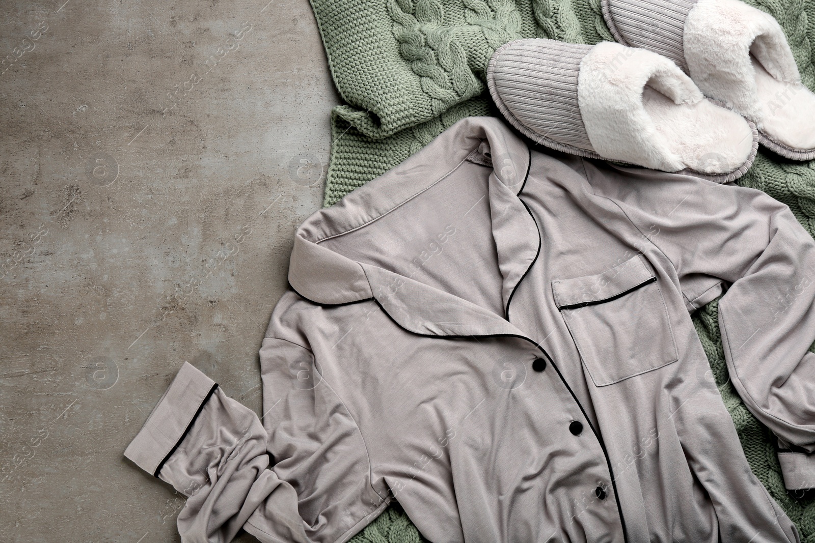 Photo of Pair of slippers, pajamas and knitted blanket on grey background, flat lay. Comfortable home outfit