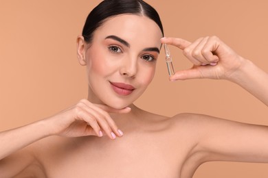 Beautiful young woman holding skincare ampoule on beige background