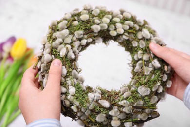 Photo of Woman holding wreath made of beautiful willow branches on blurred background, closeup