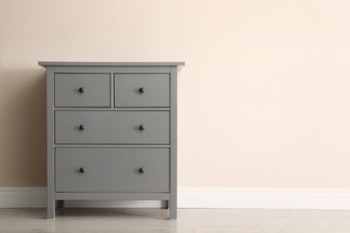 Photo of Grey chest of drawers near beige wall. Space for text