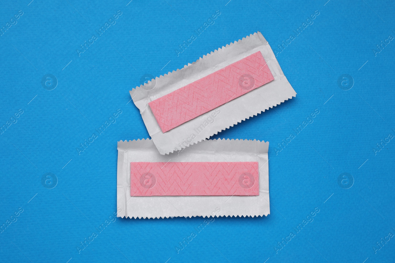 Photo of Unwrapped sticks of chewing gum on light blue background, flat lay