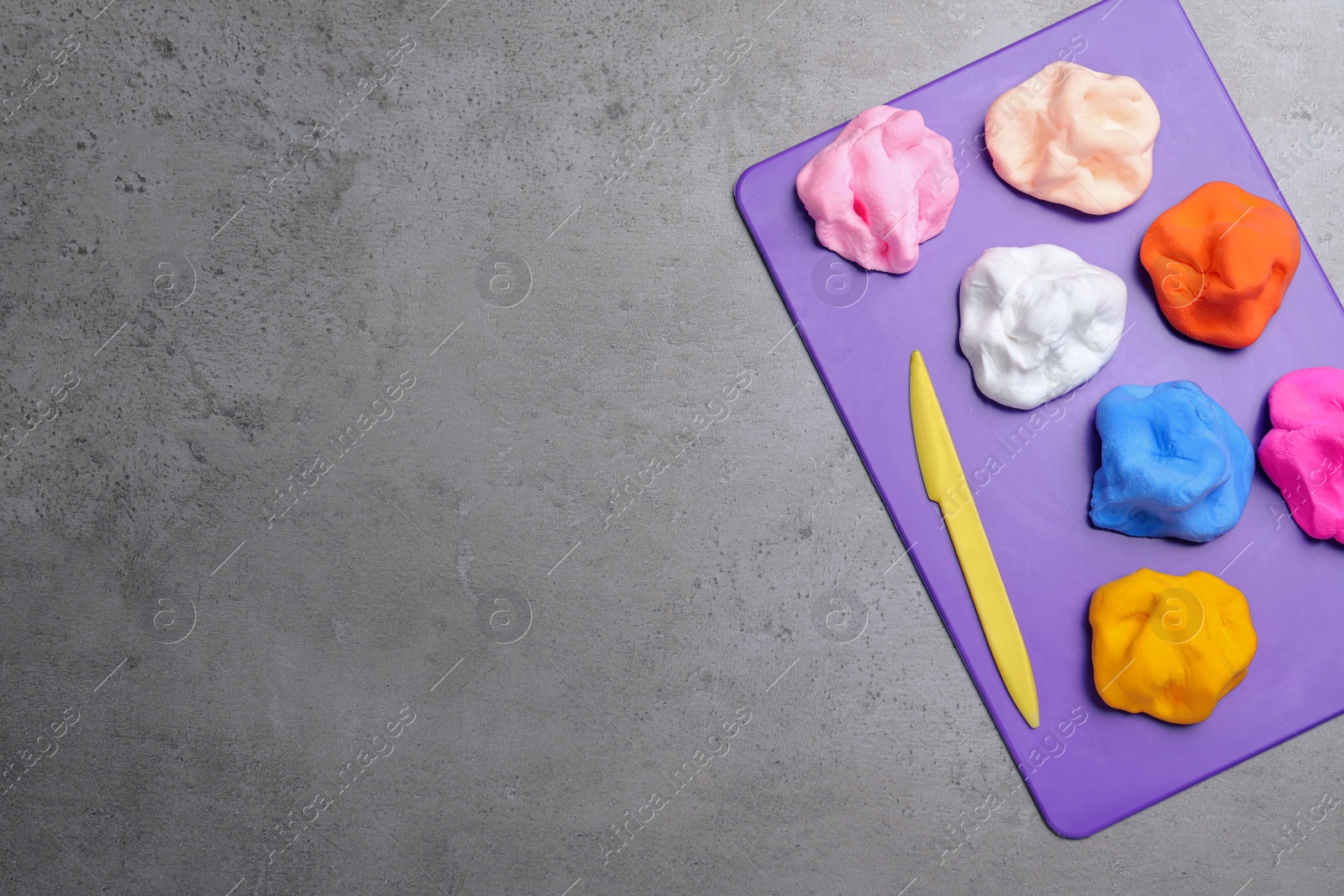 Photo of Many different colorful plasticine pieces with knife on grey table, top view. Space for text