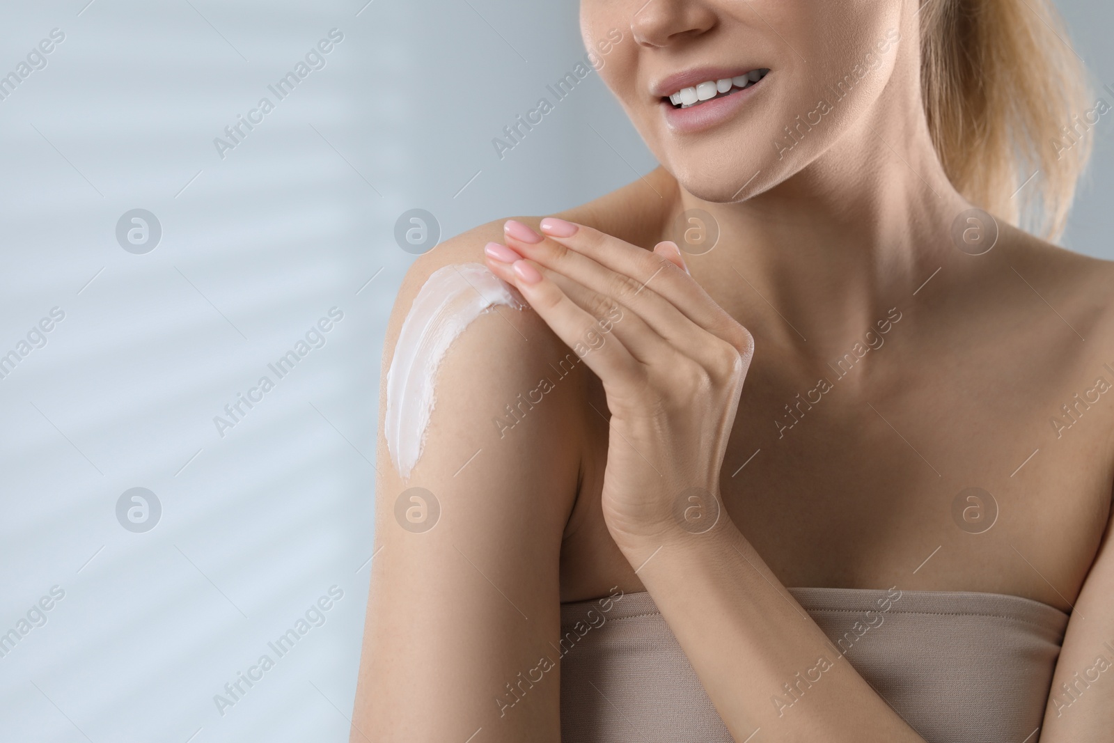 Photo of Woman applying body cream onto shoulder on light grey background, closeup. Space for text