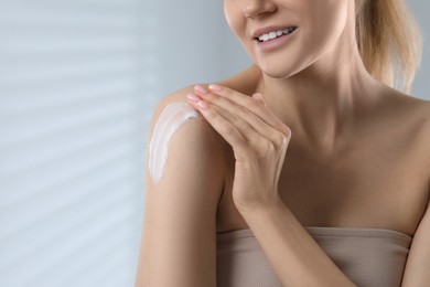 Woman applying body cream onto shoulder on light grey background, closeup. Space for text