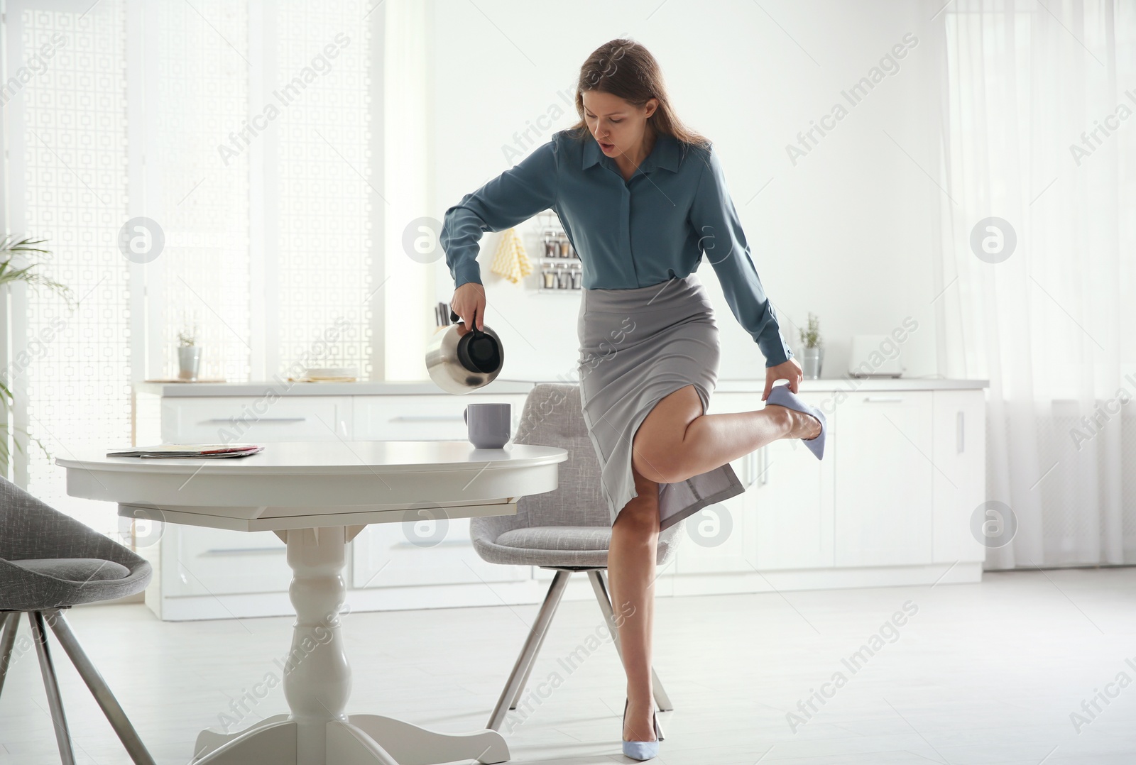 Photo of Young woman pouring coffee into cup while putting on shoes at home in morning