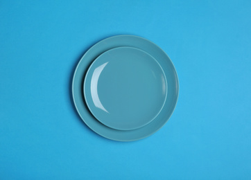 Photo of Clean empty plates on blue background, top view