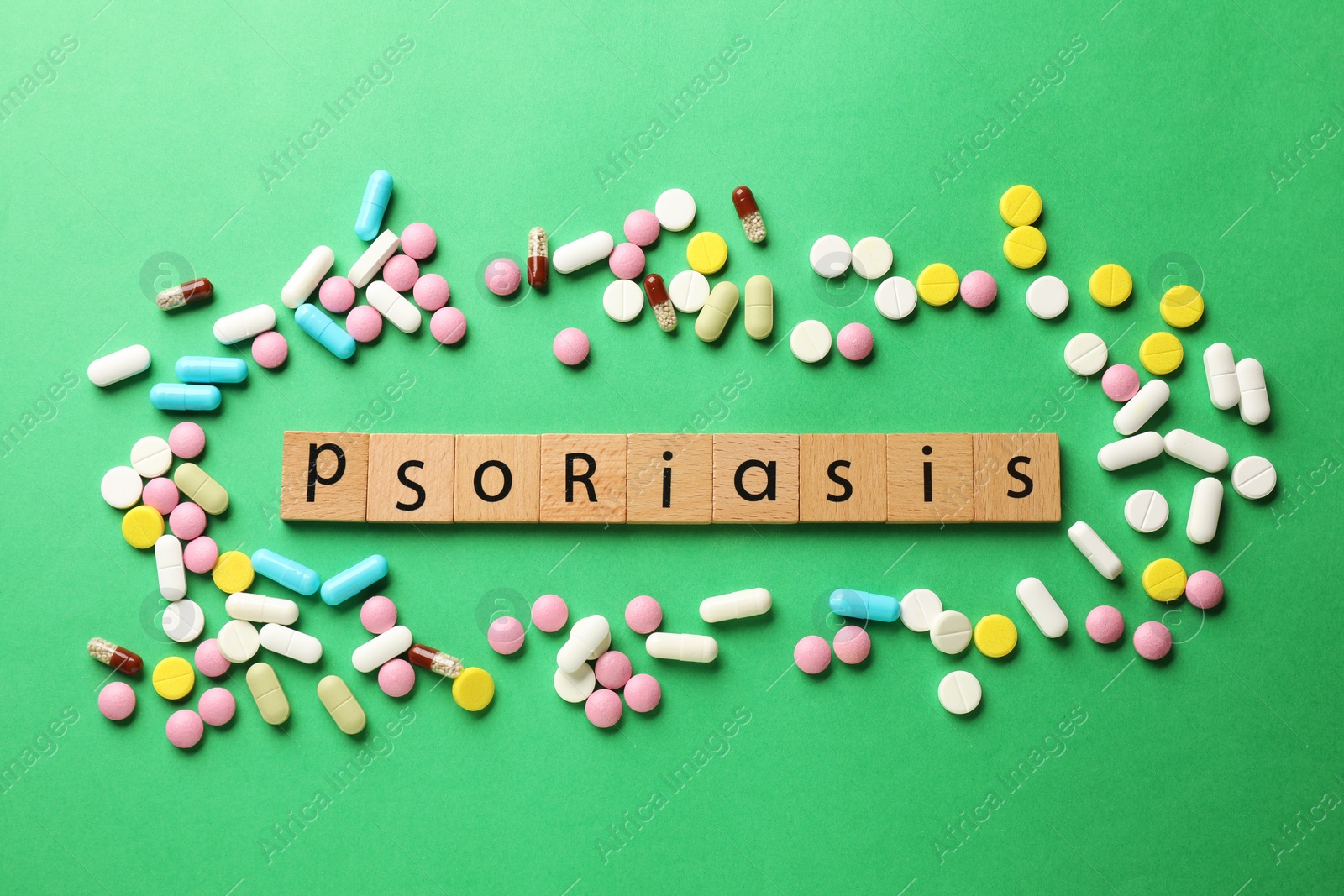 Photo of Word Psoriasis made of wooden squares with letters and different pills on green background, flat lay