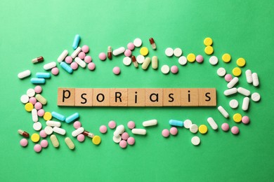 Word Psoriasis made of wooden squares with letters and different pills on green background, flat lay