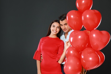 Photo of Beautiful couple with heart shaped balloons on dark background, space for text