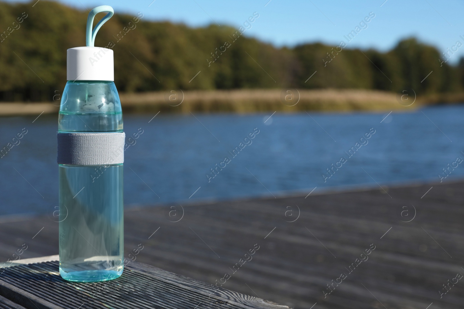 Photo of Glass bottle with water on wooden pier near river outdoors. Space for text