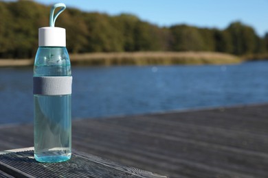 Photo of Glass bottle with water on wooden pier near river outdoors. Space for text