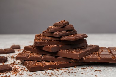Photo of Pieces and shavings of tasty chocolate on light grey table, closeup