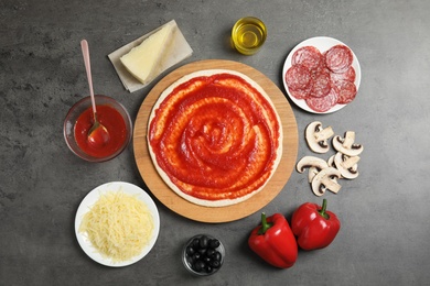 Flat lay composition with pizza crust and ingredients on grey table