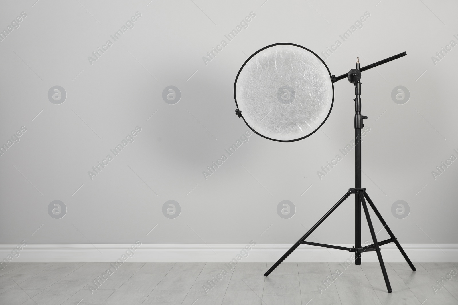 Photo of Studio reflector on tripod near grey wall in room, space for text. Professional photographer's equipment