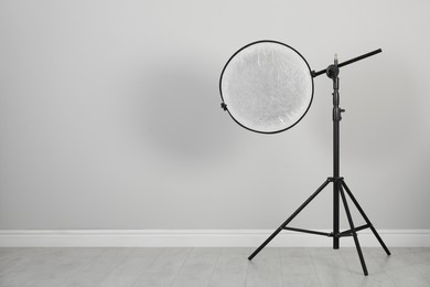 Studio reflector on tripod near grey wall in room, space for text. Professional photographer's equipment