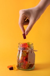 Woman taking gummy bear candy from glass jar on yellow background, closeup