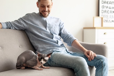 Photo of Young man with cute cat on sofa at home