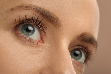 Photo of Woman showing difference in eyelashes length after mascara applying against light brown, closeup