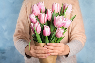 Woman with beautiful pink spring tulips on light blue background, closeup