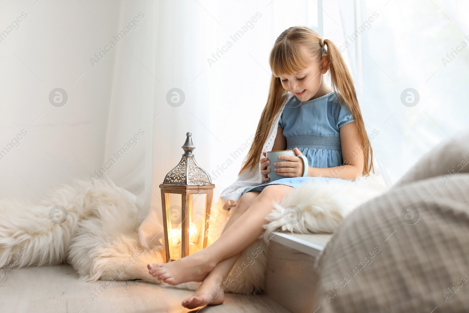 Photo of Cute little child with cup of cocoa sitting on windowsill at home. Christmas celebration