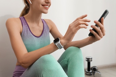 Photo of Young woman with modern smart watch and phone indoors, closeup
