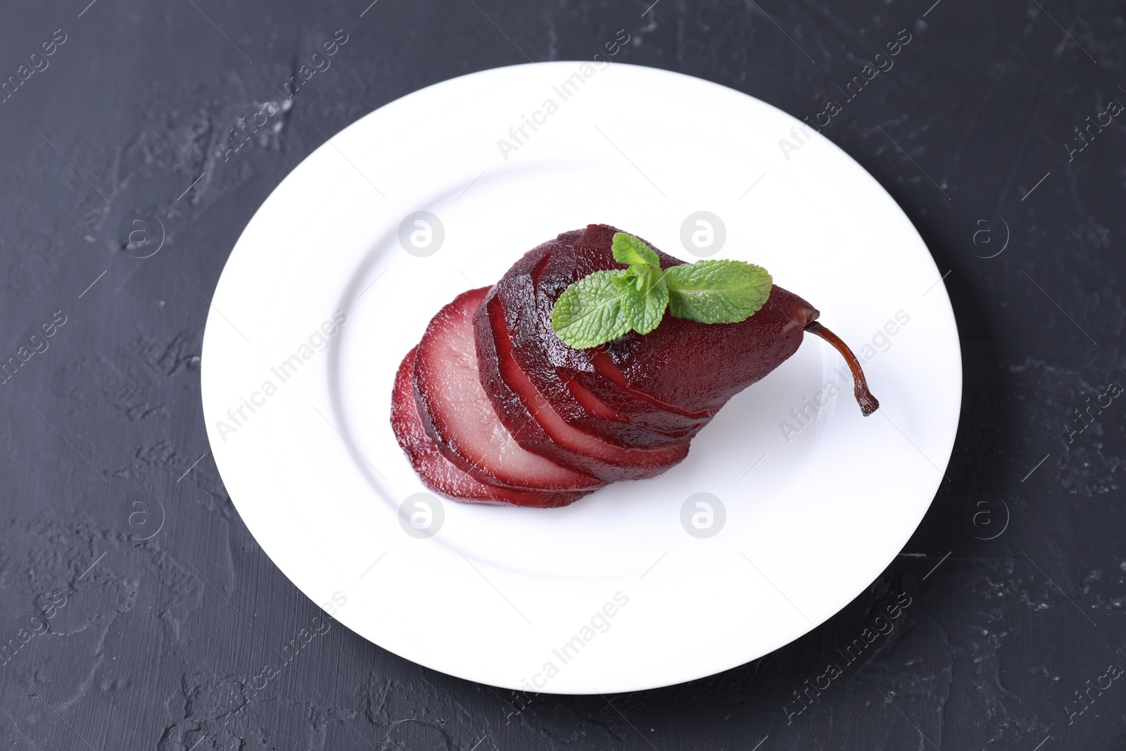 Photo of Tasty red wine poached pear and mint on black table, above view